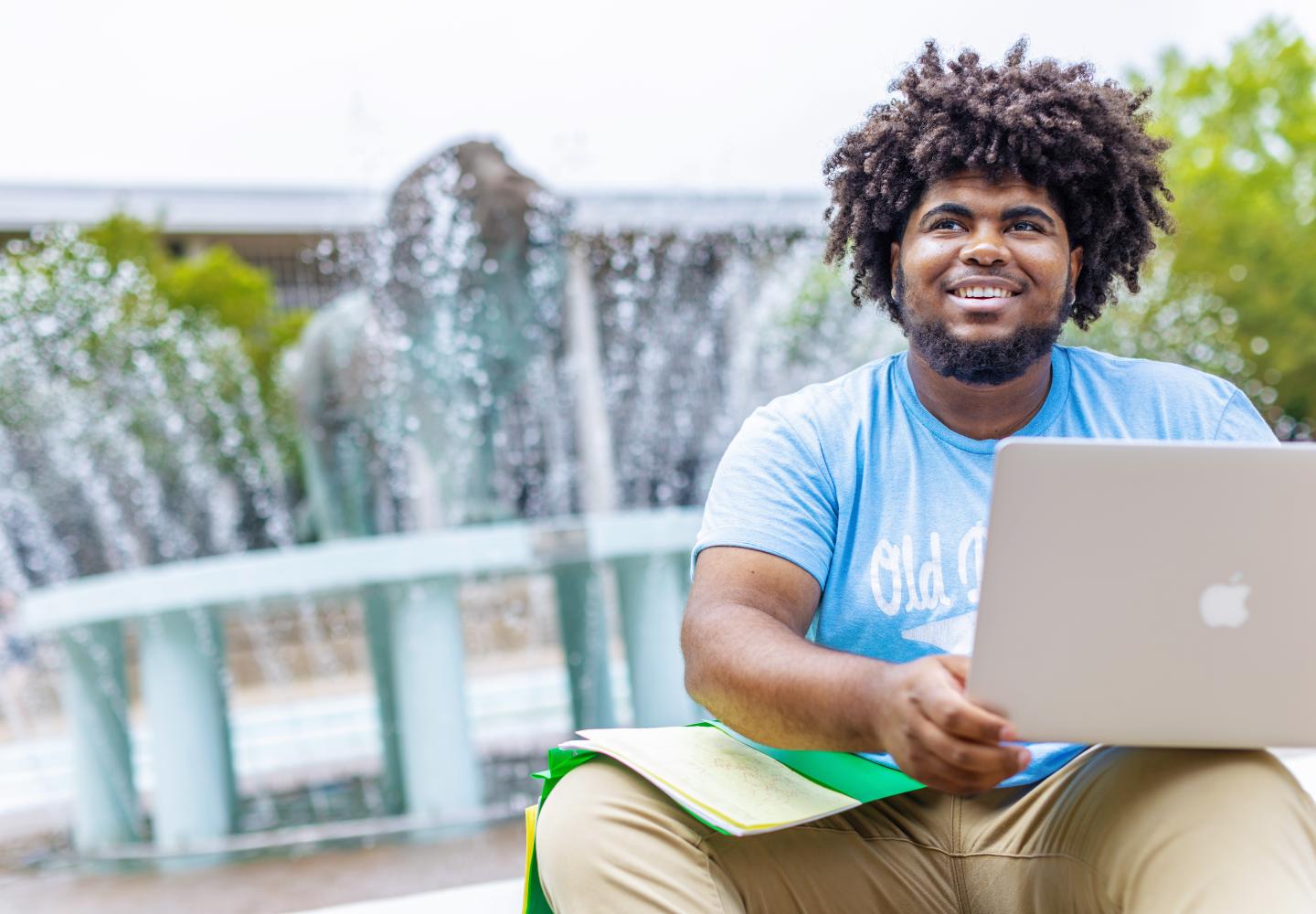 an 鶹AV student is sitting in front of the lion fountain with a laptop