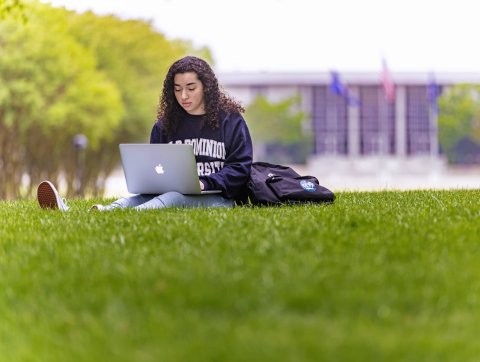 A female student wearing an 鶹AV sweatshirt is studying on Kaufman Mall with her laptop resting on her legs